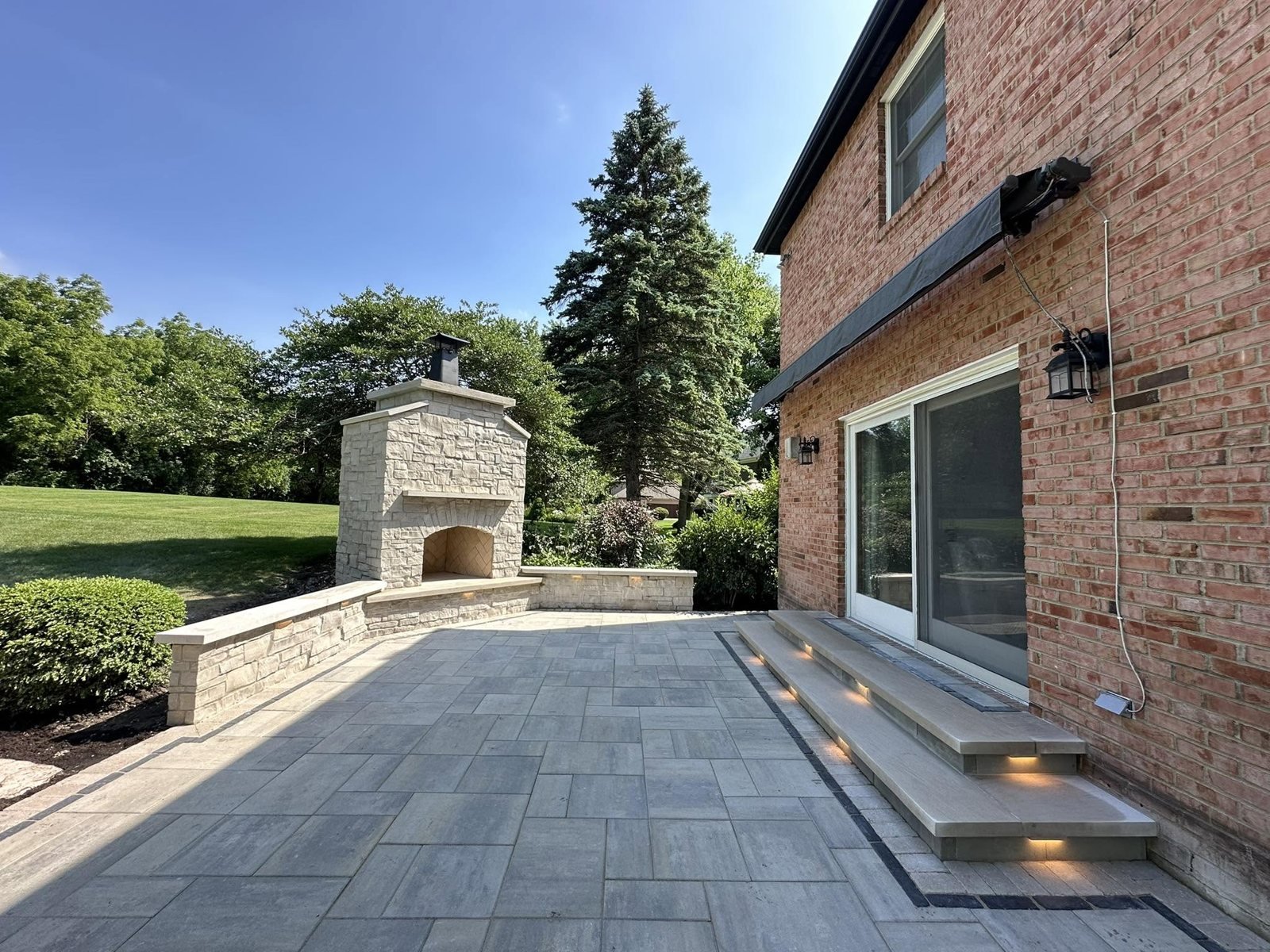Finished paver patio with stone fireplace and lit steps
